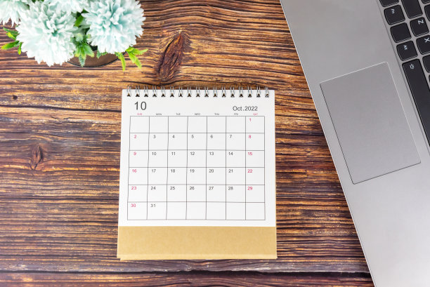 2022年10月日历日期笔记本电脑和蓝色的花在黑色的花瓶在质朴的木桌上。图片下载