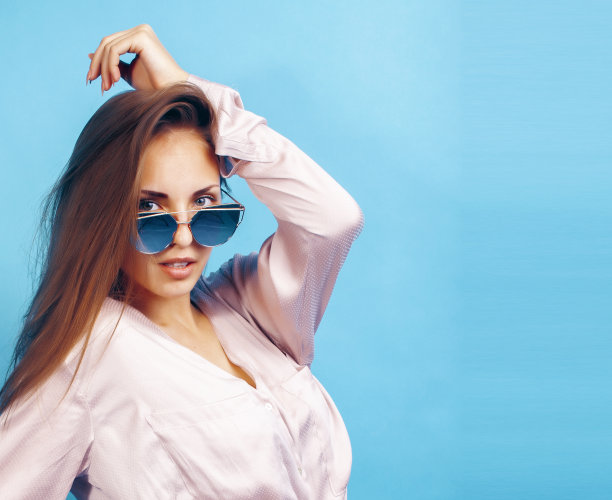 年轻漂亮的女孩戴着太阳镜在蓝色的背景上摆出快乐的微笑，生活方式的人在夏天度假的概念图片下载