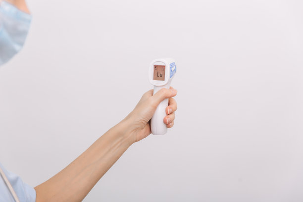 医生手中的测温枪。近距离拍摄的医生戴着防护外科口罩，准备使用红外等距温度计枪检查体温的病毒症状图片下载
