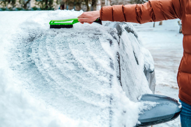 一名男子手里拿着一把刷子，正在擦车窗上的雪。交通的概念，冬天，天气，人和车辆。图片下载