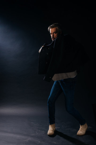 一名穿着正式、头发灰白的英俊成年男子在黑色背景的工作室里摆姿势的肖像。图片下载