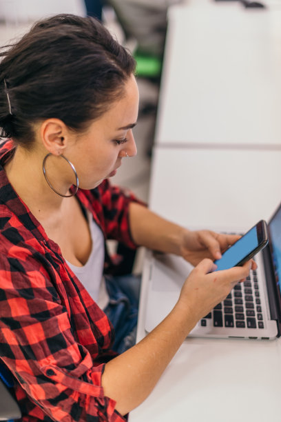 使用笔记本电脑的美丽女人在看智能手机的侧面特写图片下载
