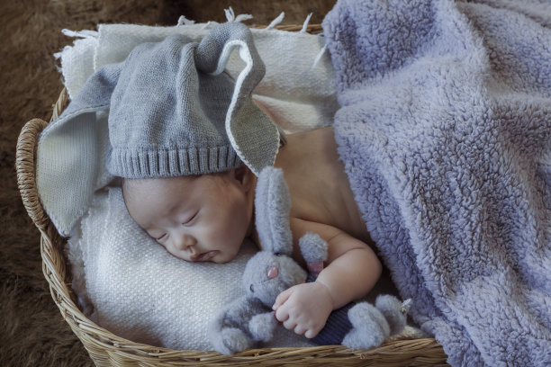 可爱的亚洲新生儿。戴一只蓝色的兔子睡个好觉。抱着兔儿爷。躺在柳条篮子里图片下载