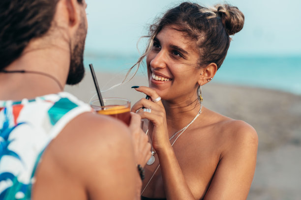迷人的年轻夫妇带着酒精鸡尾酒在海滩上散步图片下载