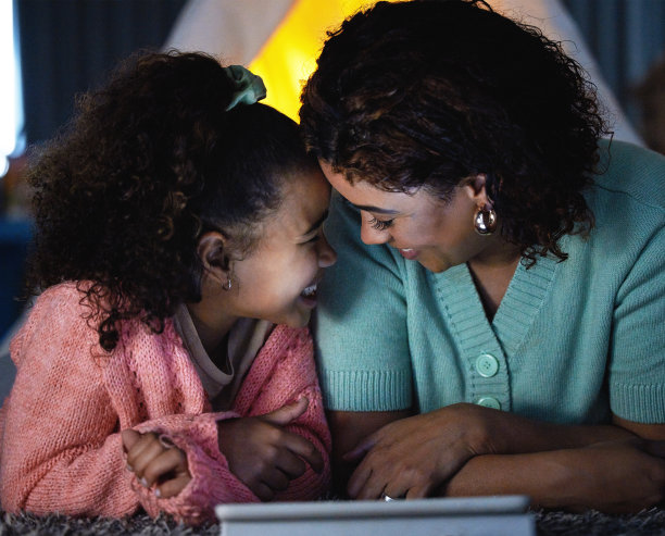 这张照片拍摄的是一个可爱的小女孩在家里睡觉的时候和妈妈一起使用数码平板电脑图片下载