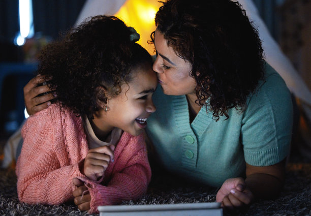 这张照片拍摄的是一个可爱的小女孩在家里睡觉的时候和妈妈一起使用数码平板电脑图片下载