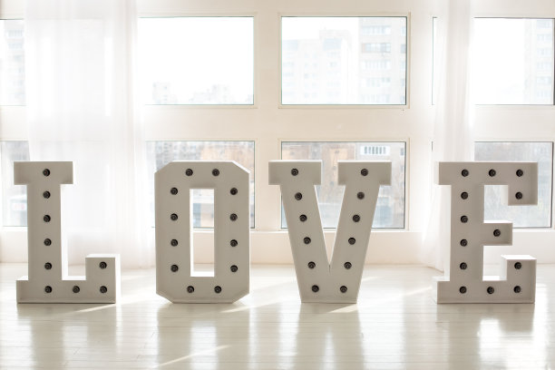 窗户旁边用大字体写着“爱”的标志。喜欢大大的白色字母和发光的led复古灯泡。情人节，2月14日。“爱”字用大号字母写。铭文是爱。婚礼装饰图片下载