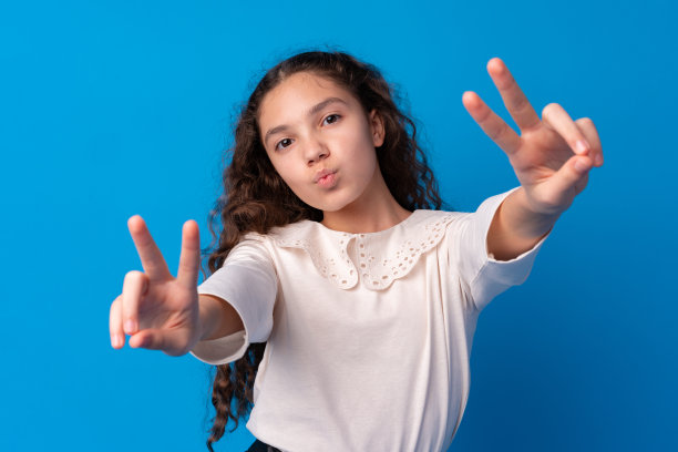 年轻女孩在蓝色背景下手势“V”图片下载