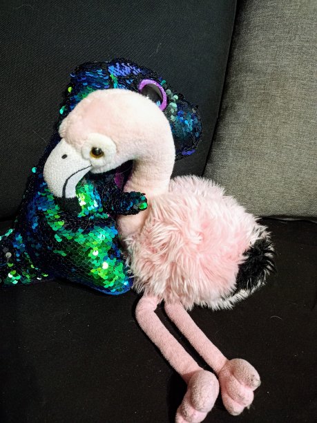 两个孩子的软玩具，一只闪亮的恐龙和一只火烈鸟在沙发上拥抱的照片图片下载