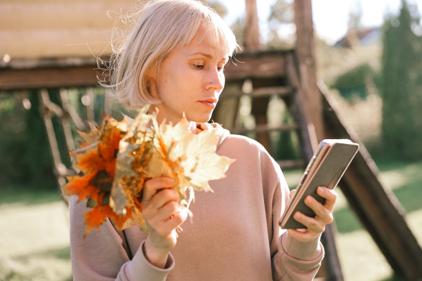 快乐的年轻漂亮的女人在户外散步在秋天的公园里用手机聊天。图片下载