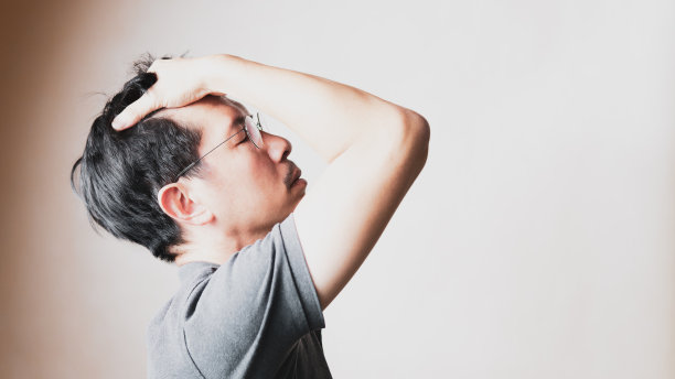 英俊的中年亚洲男人独自站着，把手放在头上，脸朝上，眼睛闭在棕色的墙壁背景上。图片下载