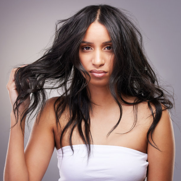 这张照片拍摄的是一个迷人的年轻女子独自站在工作室里，看着自己的头发感到沮丧图片下载