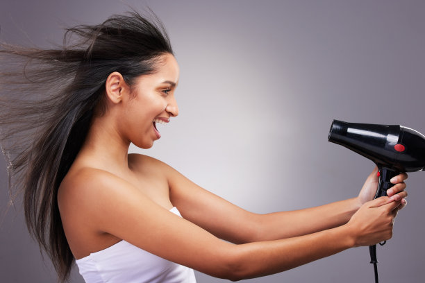 一个迷人的年轻女子独自站在工作室里，玩着吹风机图片下载