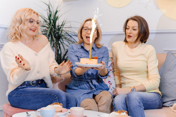 一群年轻快乐的妇女高兴地庆祝新的成就。桌上放着蛋糕、蜡烛和一杯茶图片下载