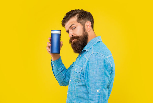 成熟野蛮的大胡子男人拿着香波瓶对着黄色背景进行护肤图片下载