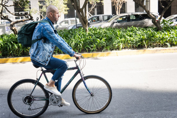 一个穿着休闲的秃头年轻人在城市里骑着自行车图片下载