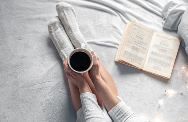 一杯咖啡在女性手中，在床上，俯视图。图片下载