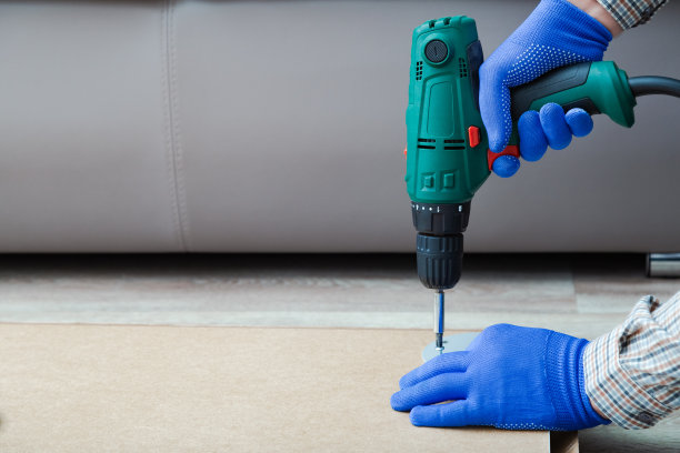 电钻在勤杂工手里工作。男性手戴手套，在家用电钻工具组装和修理家具。本空间图片下载