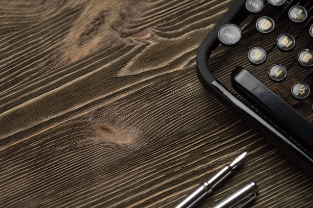 棕色的木桌上放着旧打字机和钢笔。图片下载