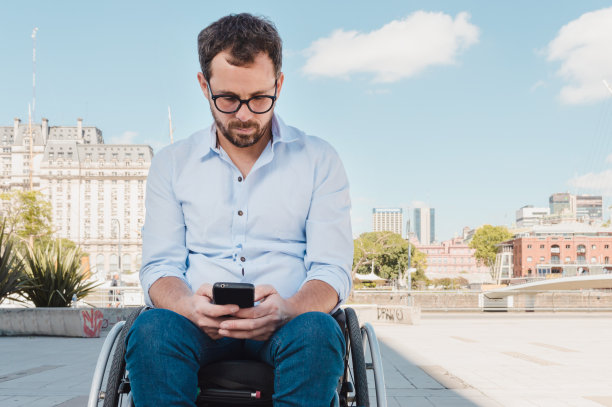 一个坐在轮椅里的成年人在外面看，用他的手机图片下载