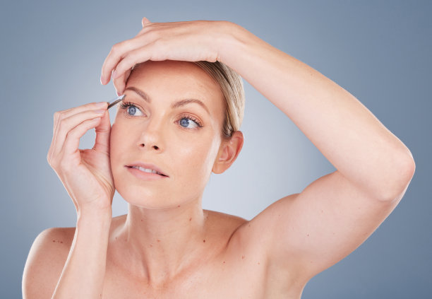 一名迷人的年轻女子在灰色背景下拔眉毛的画室照片图片下载