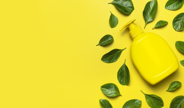 天然有机化妆品。美容，水疗，品牌模型。黄色化妆品瓶容器新鲜的绿叶在黄色背景平躺顶视图。极简概念包装生态化妆品图片下载