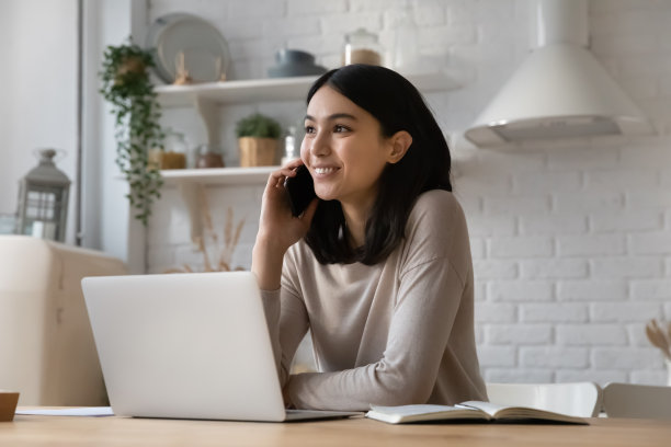 亚洲女人坐在笔记本电脑前打电话图片下载