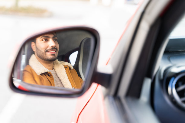 白天穿着夹克，手握方向盘，骑着车。脸在后视镜里图片下载
