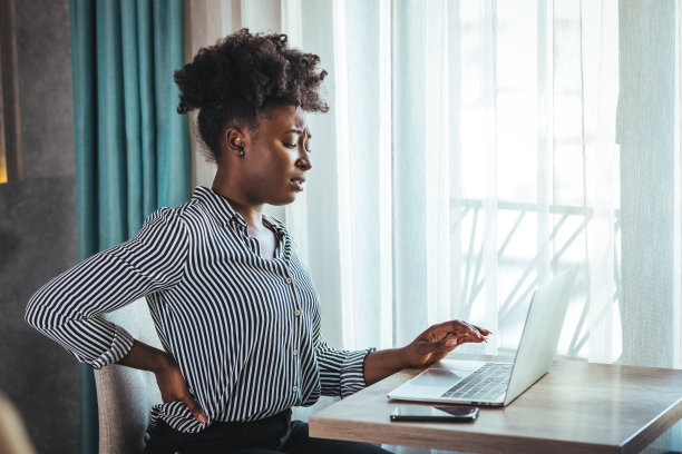 疲惫的非洲裔美国千禧一代女性员工坐在办公桌前触摸背部，遭受较低程度的脊柱痉挛图片下载