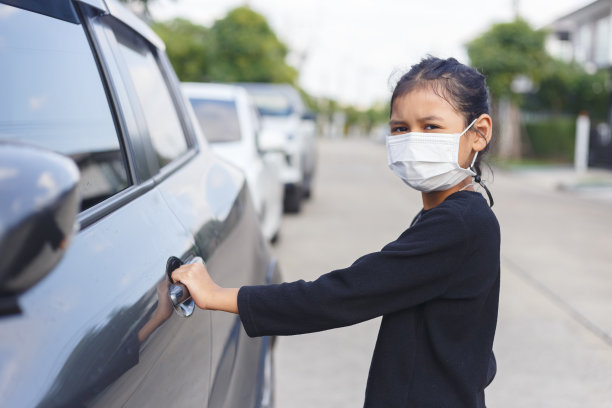 戴着面具的女孩正在开车门。2019冠状病毒病暴发期间，女童佩戴口罩。图片下载