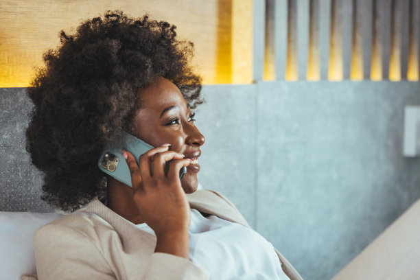 一位非洲女商人正在出差，她躺在旅馆房间的床上打电话图片下载