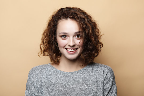人，快乐和表情的概念。漂亮年轻的卷发女人可爱的微笑独自摆姿势在米色的背景图片下载