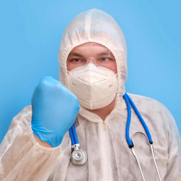 男医生，医生，穿着防护服，戴着护目镜和面罩，背景是工作室的蓝色。医护人员穿着白色抗病毒防护服，戴着N95呼吸器和安全眼镜图片下载