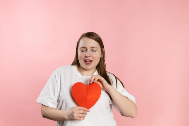 欣赏年轻女孩棕色头发，白色t恤在粉红色的背景和红色的心图片下载