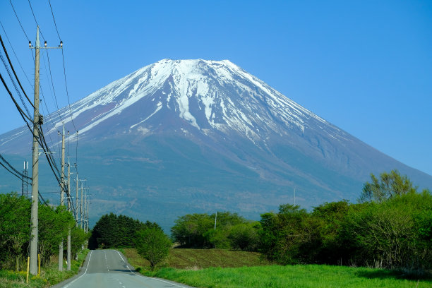 富士山在蓝天的背景下，道路在前面的道路驾驶到富士山周围的乡村地区的日本步道。图片下载