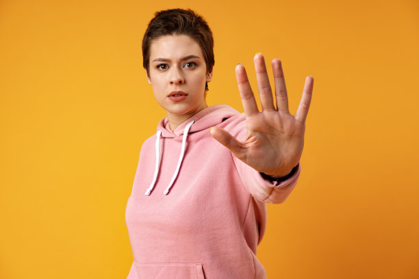 一个十几岁的女孩在黄色背景下展示停车标志的手掌图片下载