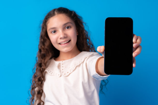 一头黑色卷发的年轻女孩在蓝色的背景下展示着智能手机屏幕图片下载