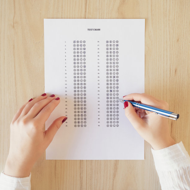 女学生的手涂着红指甲参加学校/大学的考试，写答卷或桌上有答案气泡的标准化考卷。多项选择素材图片