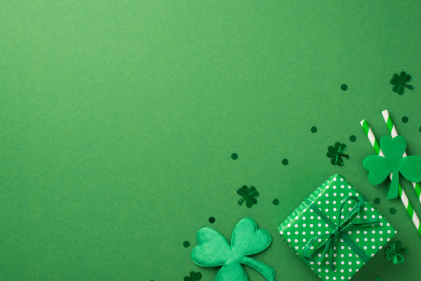 俯视图照片的礼盒与绿色丝带，两条纹吸管饮料和许多不同大小的纸屑三叶草形状和点在绿色孤立的背景copyspace图片下载