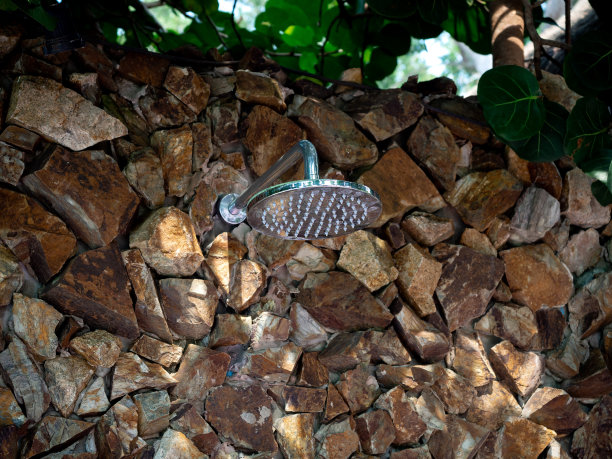 户外淋浴自然石墙和绿叶背景。游泳池淋浴，特写镜头。图片下载