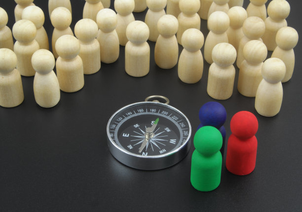 许多木制人物和彩色木制人物作为领袖站在指南针附近。图片下载