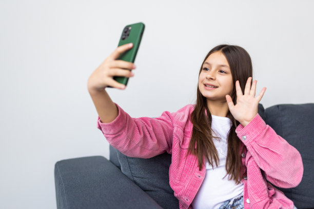 你好追随者。小女孩的全身照片学习远程休息放松使用智能手机，有在线instagram广播挥手说自己坐腿交叉舒适的沙发在房子里室内图片下载