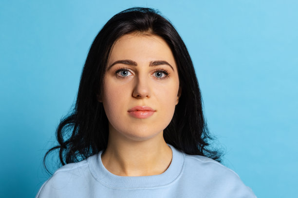 年轻美丽的女孩的肖像与长光滑的黑色头发摆孤立的蓝色背景。情感概念，面部表情图片下载