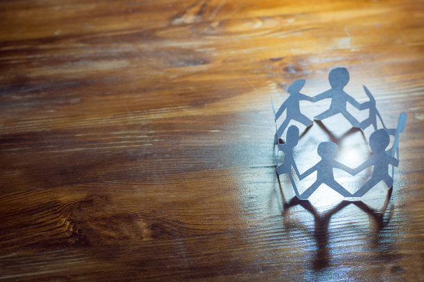 友谊是一种团队合作。纸人手牵着手站在一个木制的表面上，在一个充满光线的圆圈里。团结、家庭、团队经营、全球沟通的理念图片下载