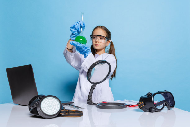 小女孩的肖像，穿着白色大礼服的孩子作为化学家，科学家的化学设备，实验室里的液体在蓝色的背景下隔离图片下载