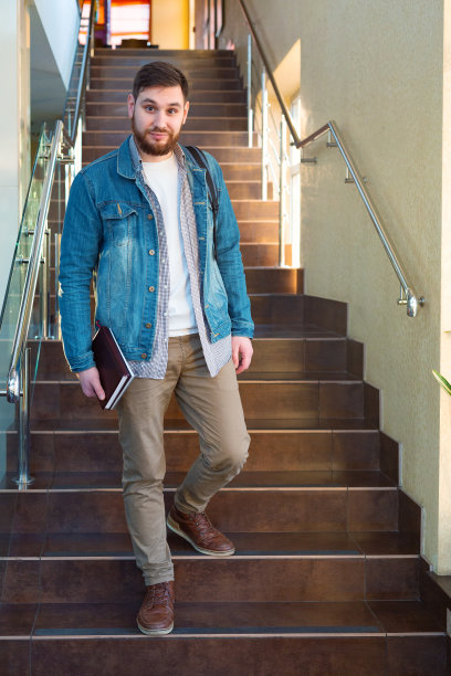 棕色楼梯上的学生。在重新开放的大学校园走廊里，一个白人英俊的大胡子男人面带微笑，背着背包笔记本。现代合作办公室的自由职业者图片下载