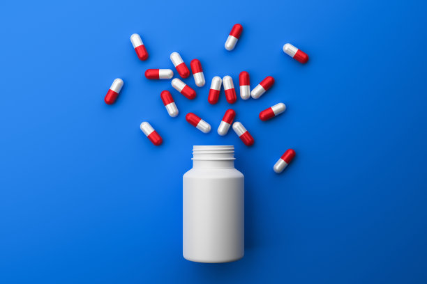 红色和白色胶囊药丸从一个塑料白色罐子在蓝色的背景俯视图。图片下载