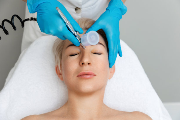 戴蓝色手套的美容师为客户的面部做气液脱皮手术。前视图。专业美容年轻化理念图片下载