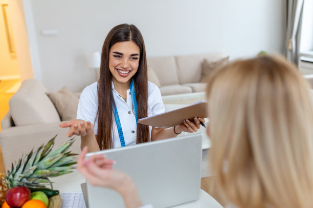医生、营养师、营养师和女患者在办公室会诊。年轻的女营养师在会诊室微笑。营养学家桌子上有健康的水果和卷尺。图片下载