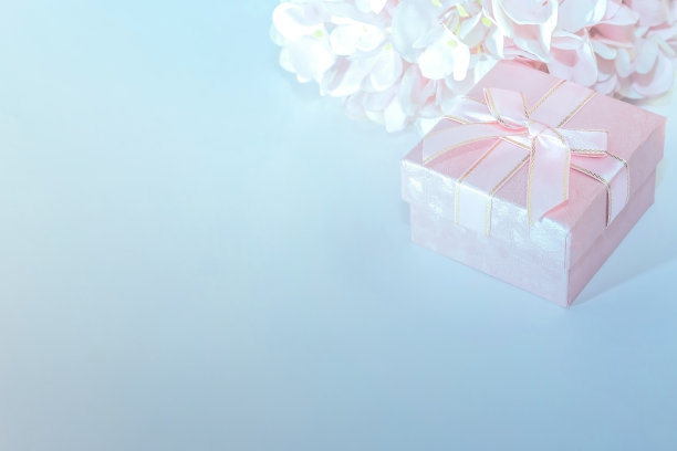 节日背景的贺卡与一个粉红色的礼品盒与蝴蝶结和花的人造绣球在柔和的颜色在蓝色的背景与复制空间图片下载